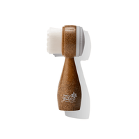 A dual-sided facial cleansing brush with soft bristles on one side and a silicone exfoliating pad on the other, featuring a wooden handle and white bristles.