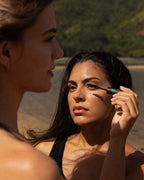 A person applying mascara to another person's eyelashes outdoors.